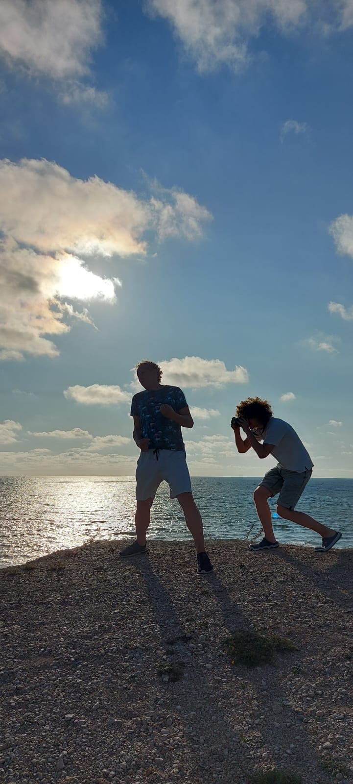 A guy taking a picture of a man on a cliff who is playing air guitar