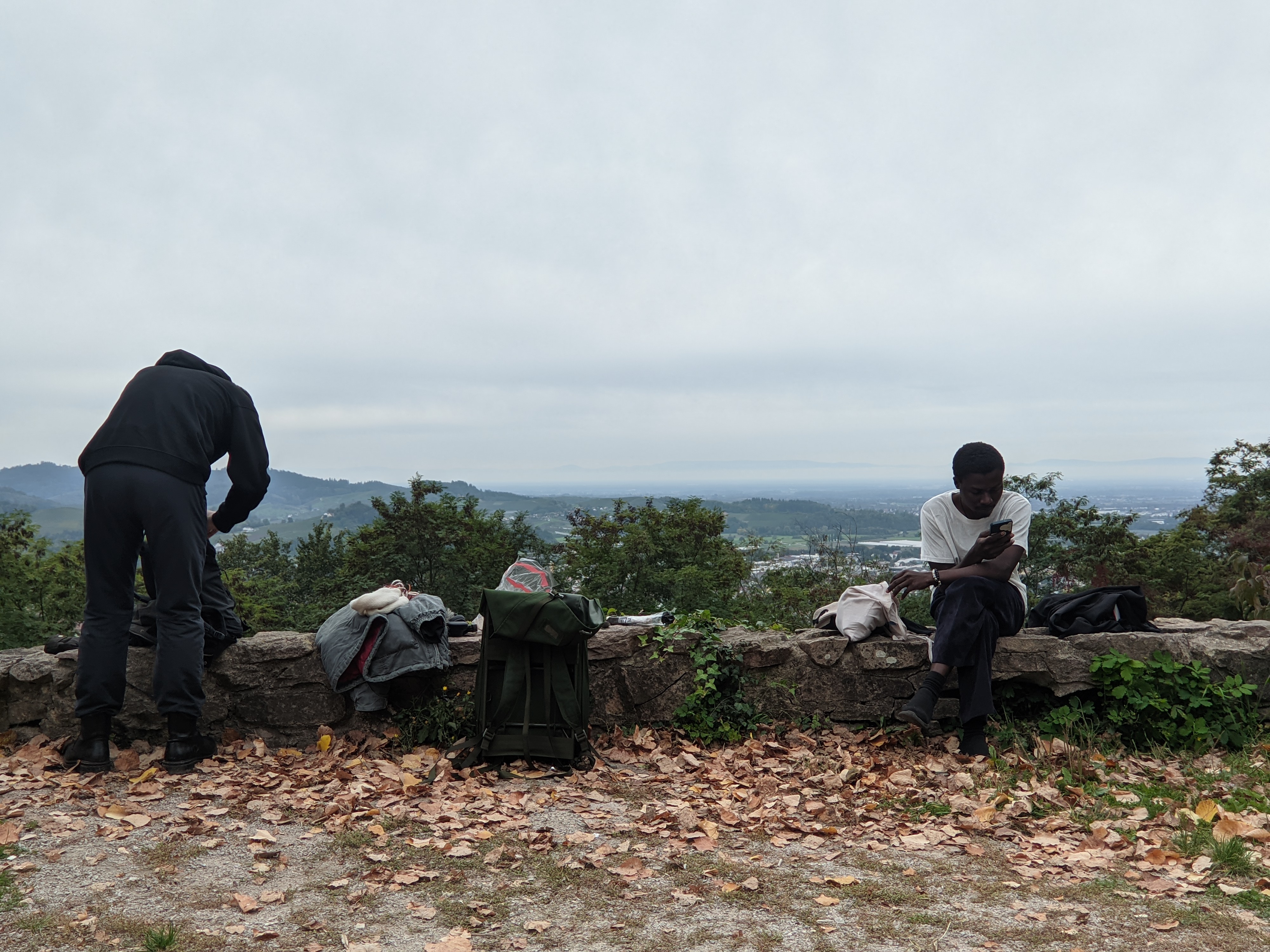Two guys on the edge of a cliff, taking a break from their hike. View of mountains in the background